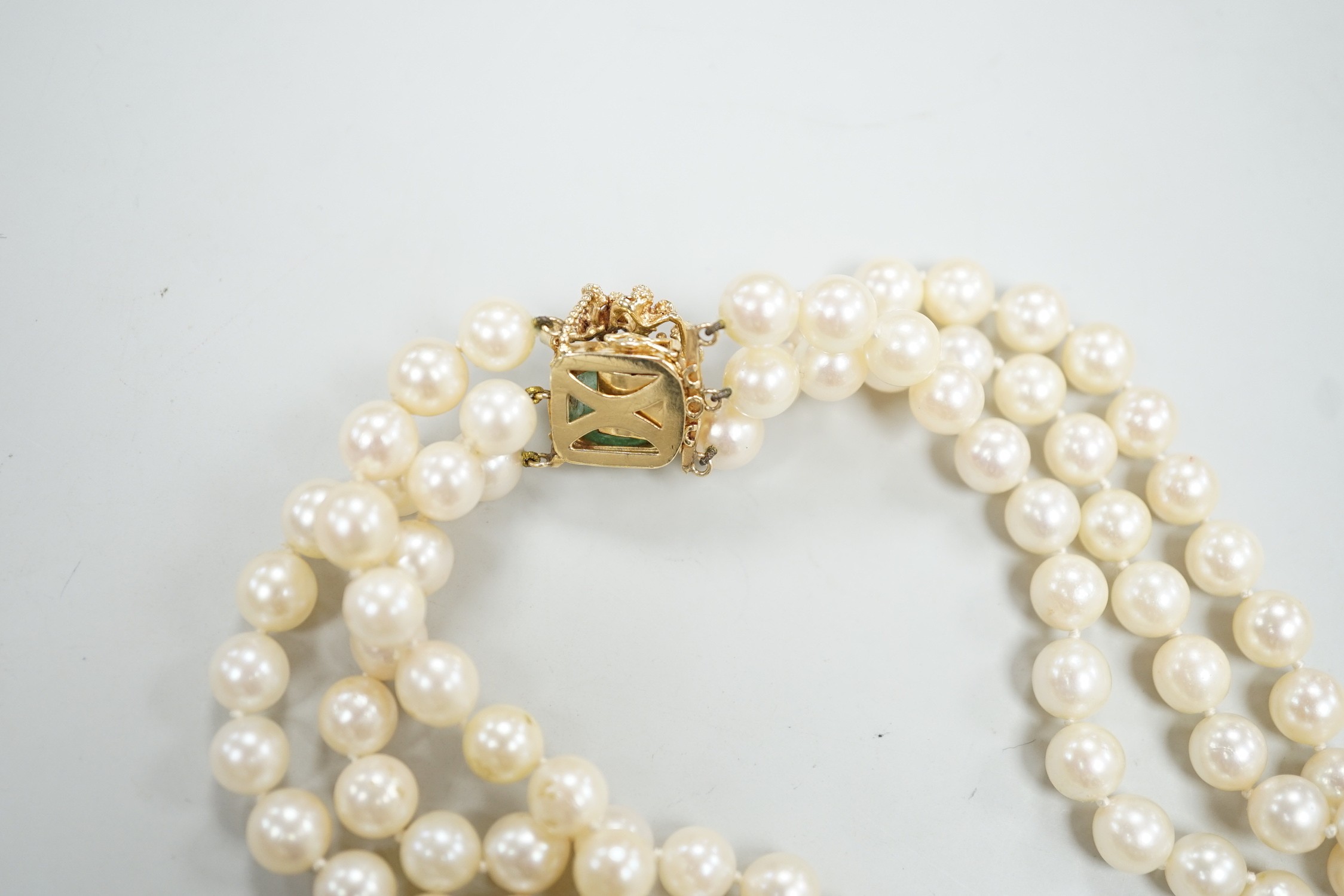 A mid to late 29th century triple strand cultured pearl choker necklace, with 14k and cabochon emerald set clasp, 34cm.